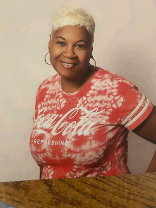 Black woman with blonde short hair smiling, wearing a shirt that says "coca-cola"
